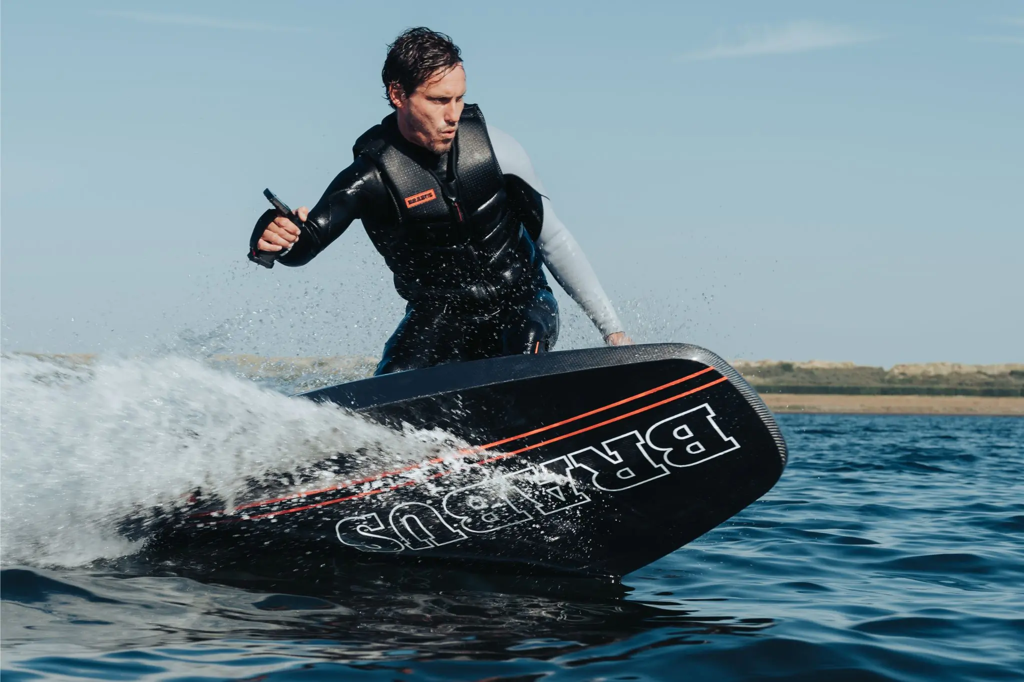 Person in life jacket rides black electric surfboard on water