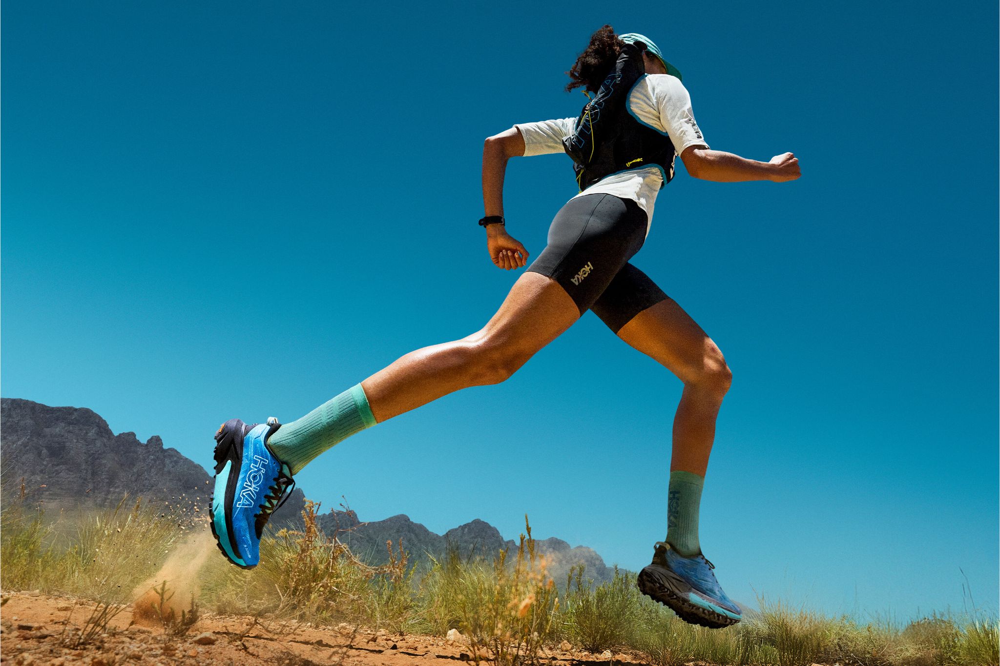 Runner in desert wearing blue hokas and running vest mid-stride