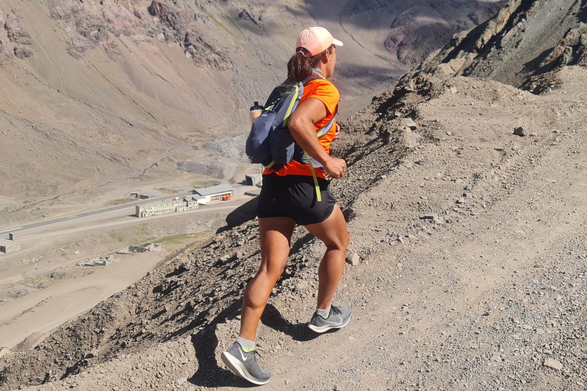 From behind, we see a person wearing a backpack running up a hill