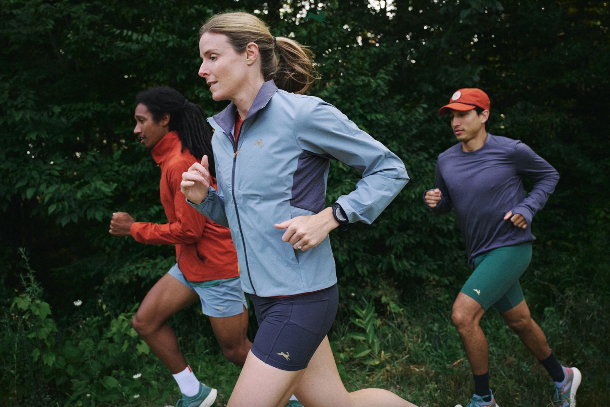 Three people run outside in forest