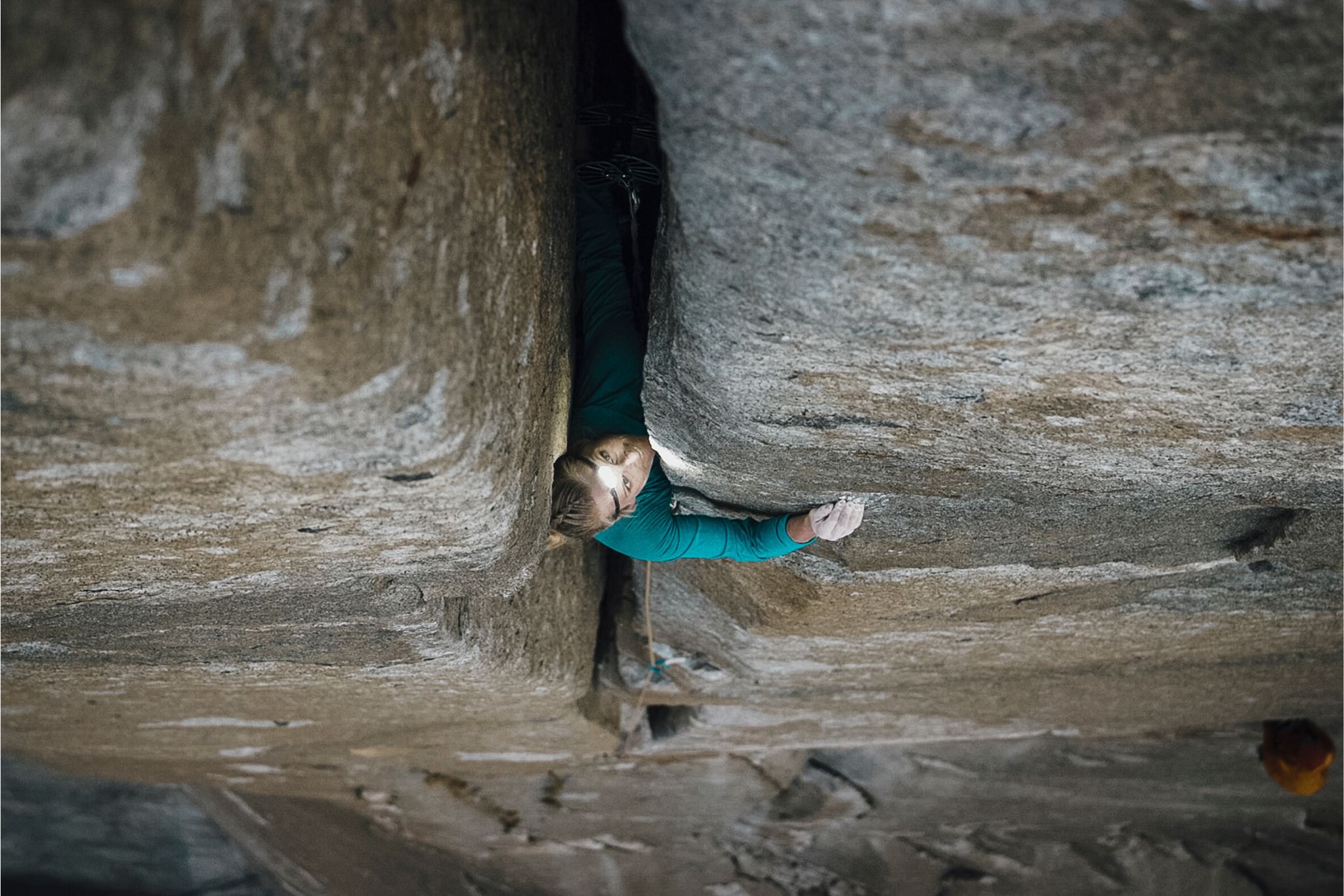 Woman in blue jacket climbs up large crack