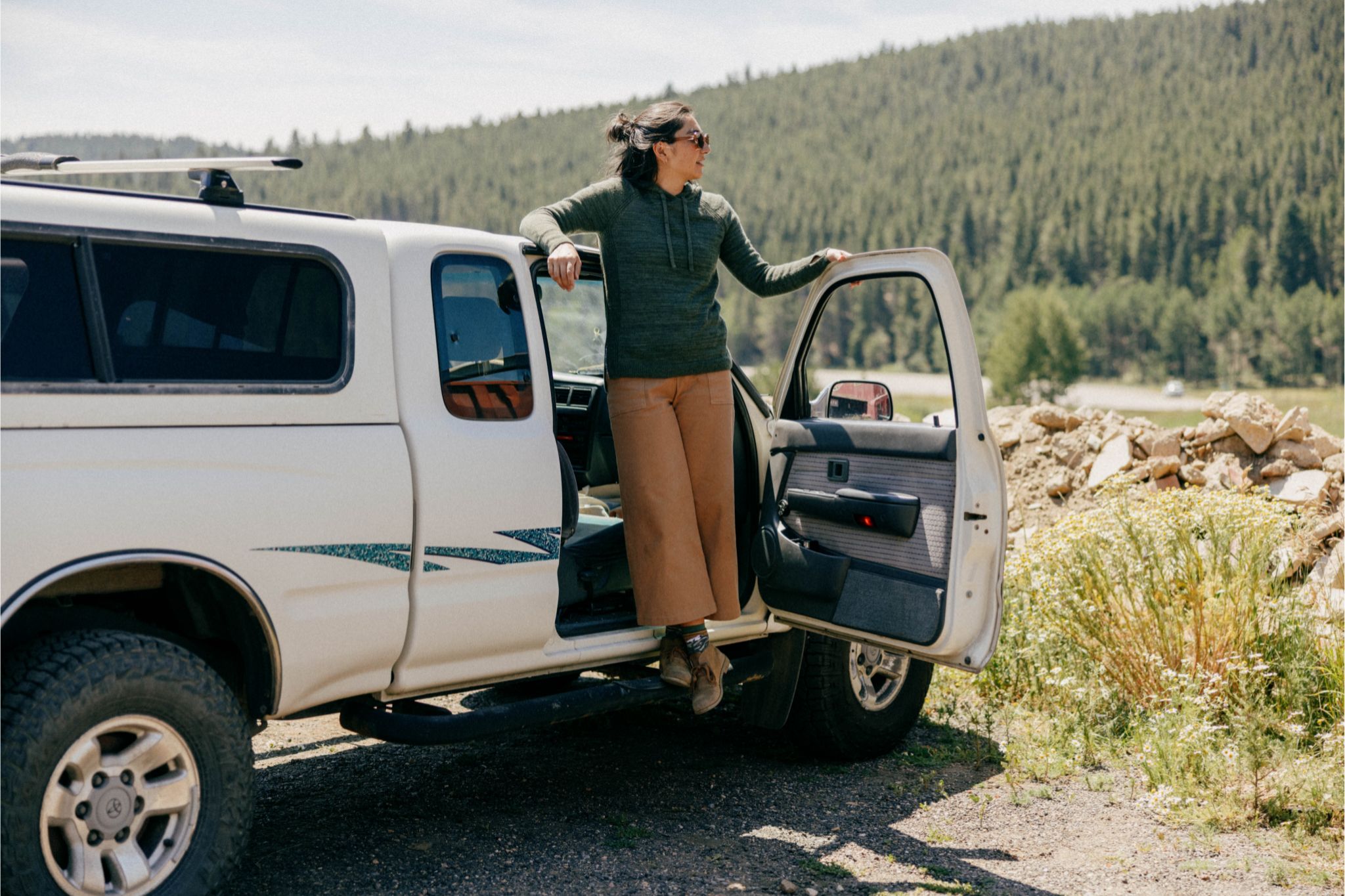 Woman in green hoodie and gray pants stands on truck