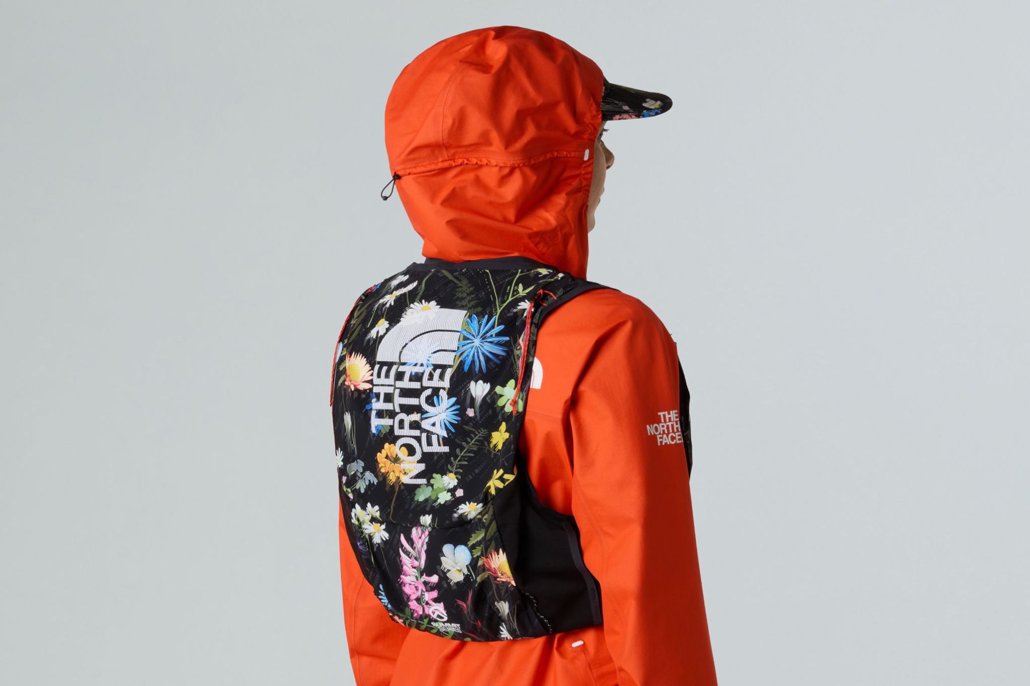 Runner wears hat, orange jacket, and floral vest with back facing camera.