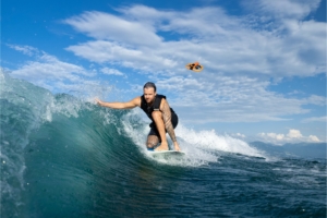 Man surfs ocean wave with orange drone behind him