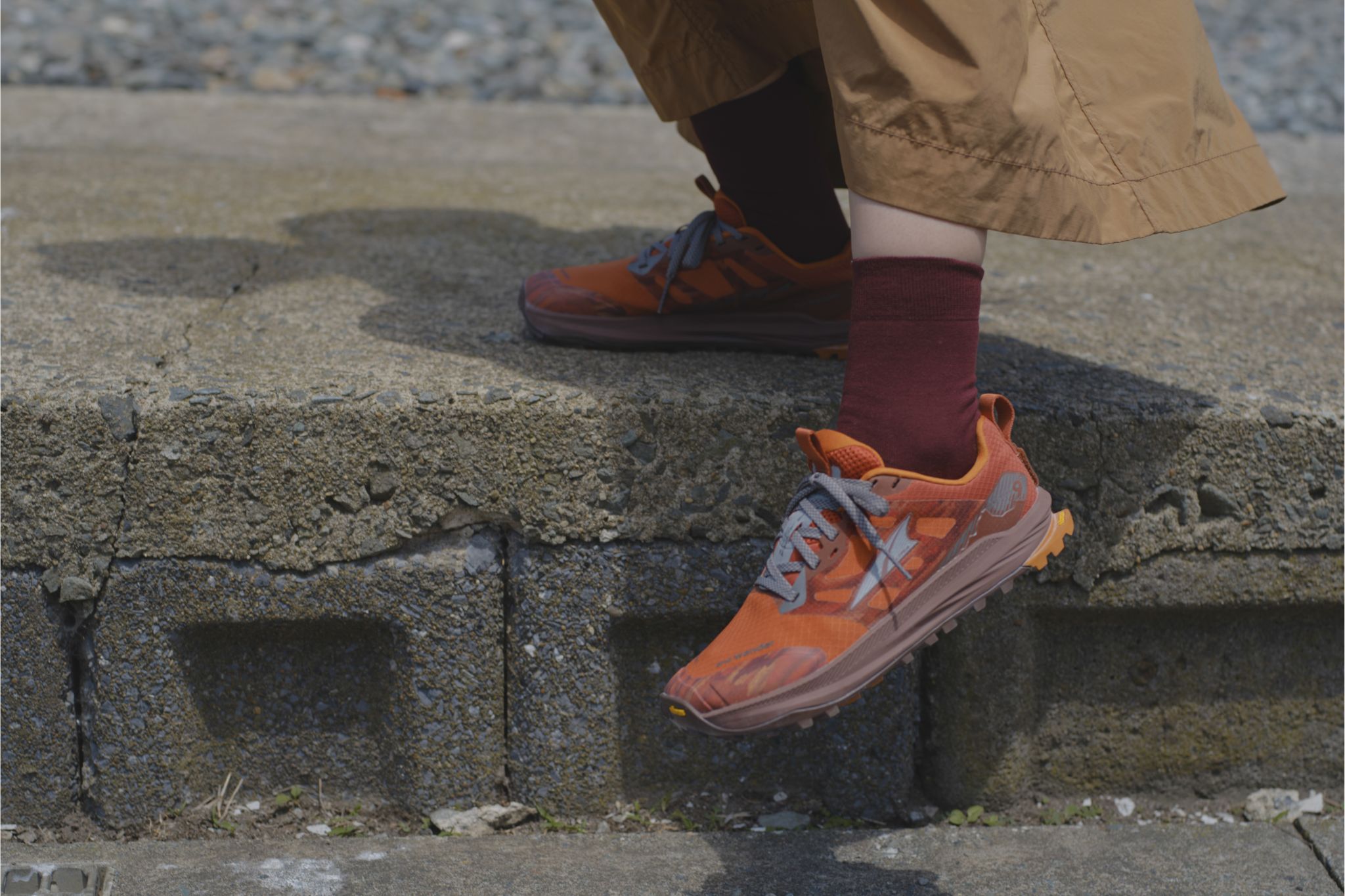 Close-up of person wearing brown pants, red socks, and orange sneakers stepping off of curb