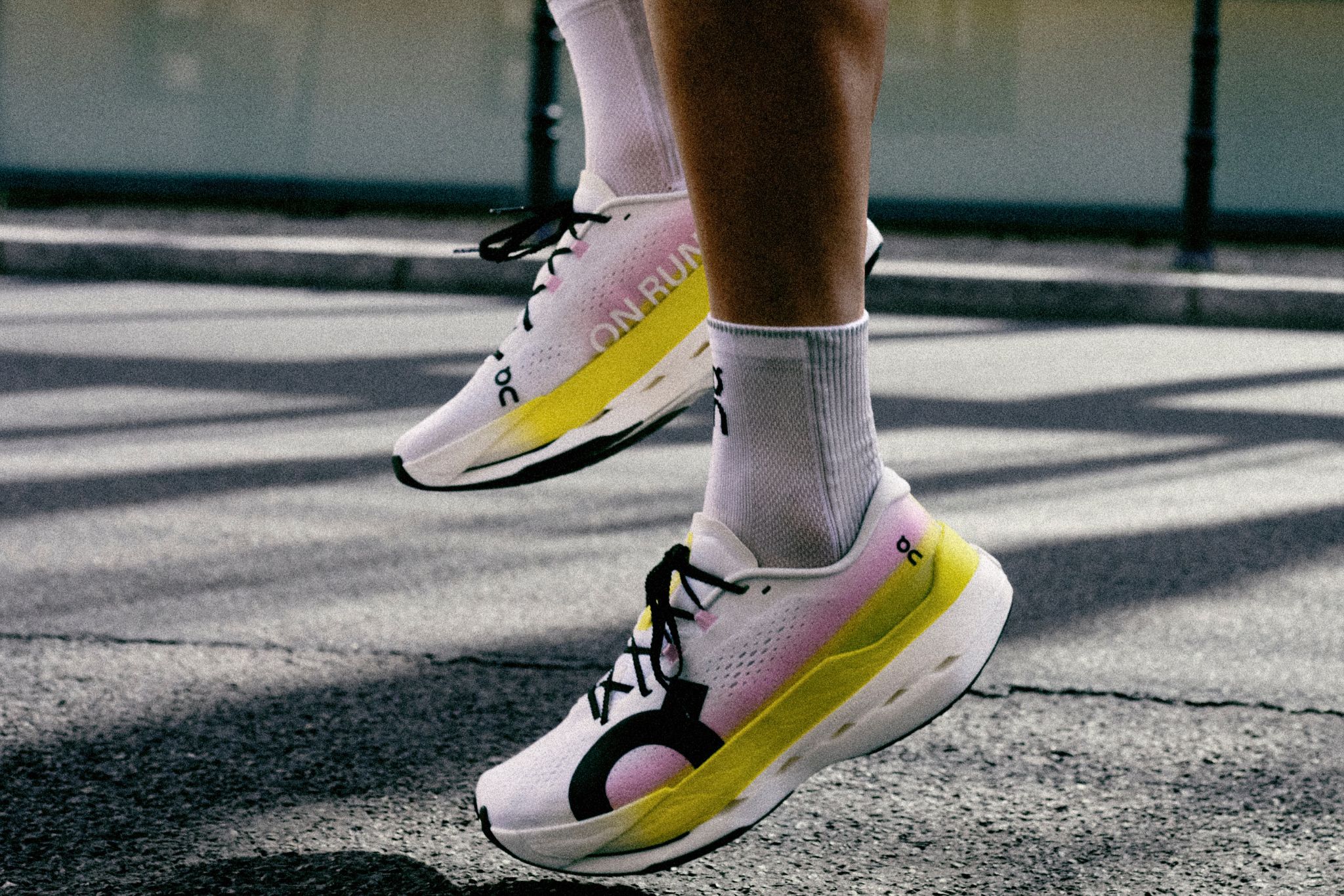 Close-up of person wearing white, yellow, and pink On running shoes.