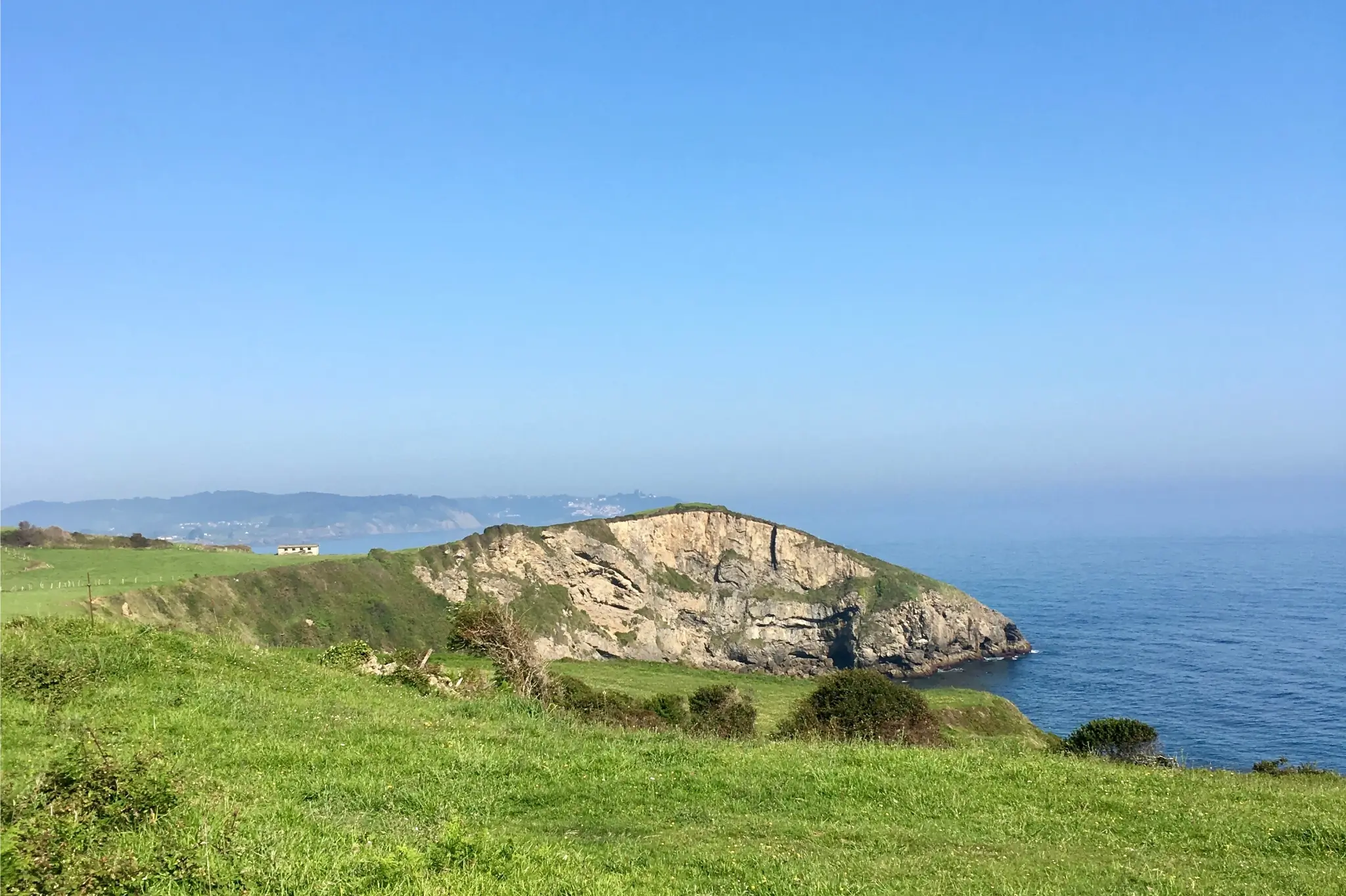 Grass hill overlooks rocky outcropping and ocean