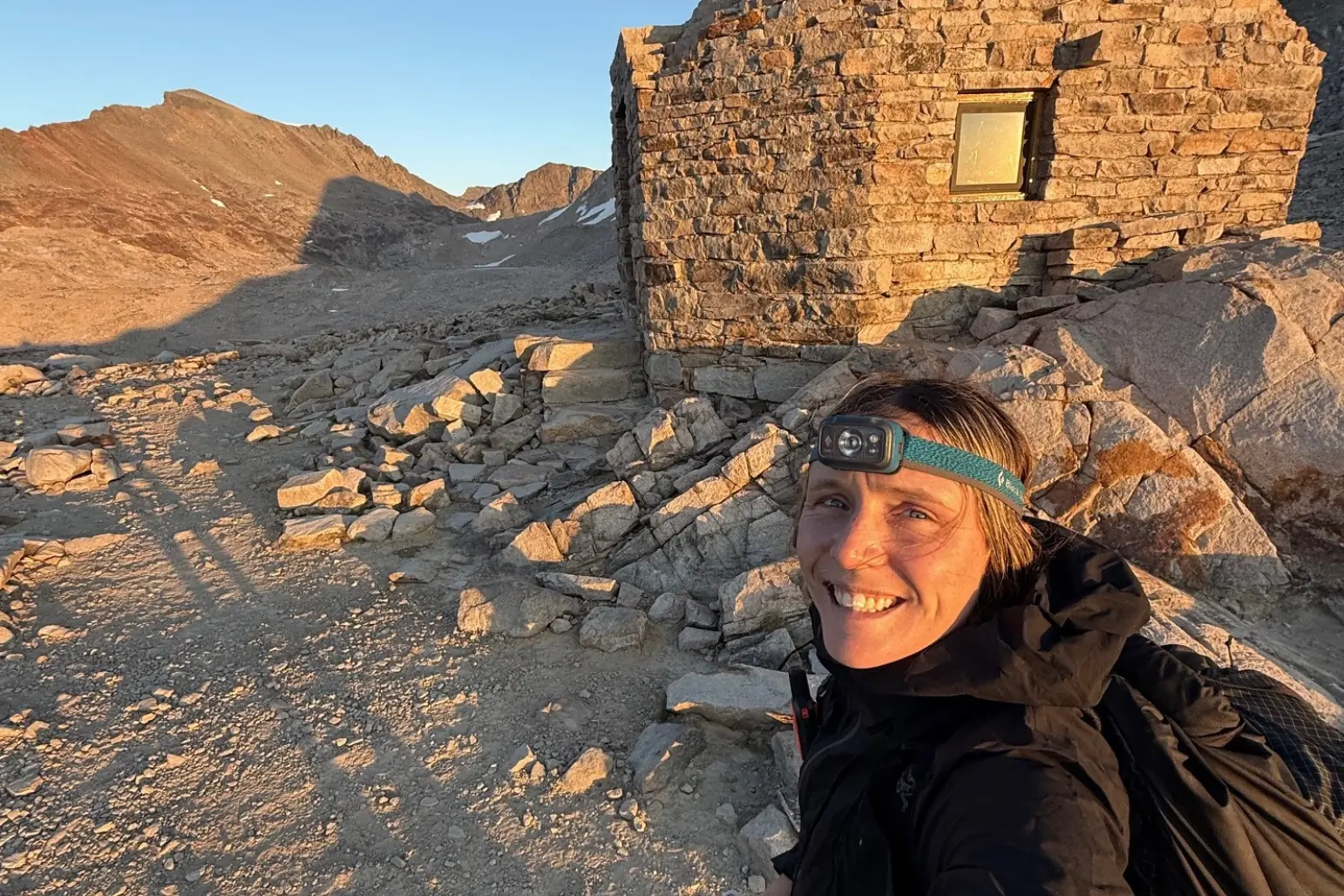 Person wearing headlamp stands in front of rocky structure