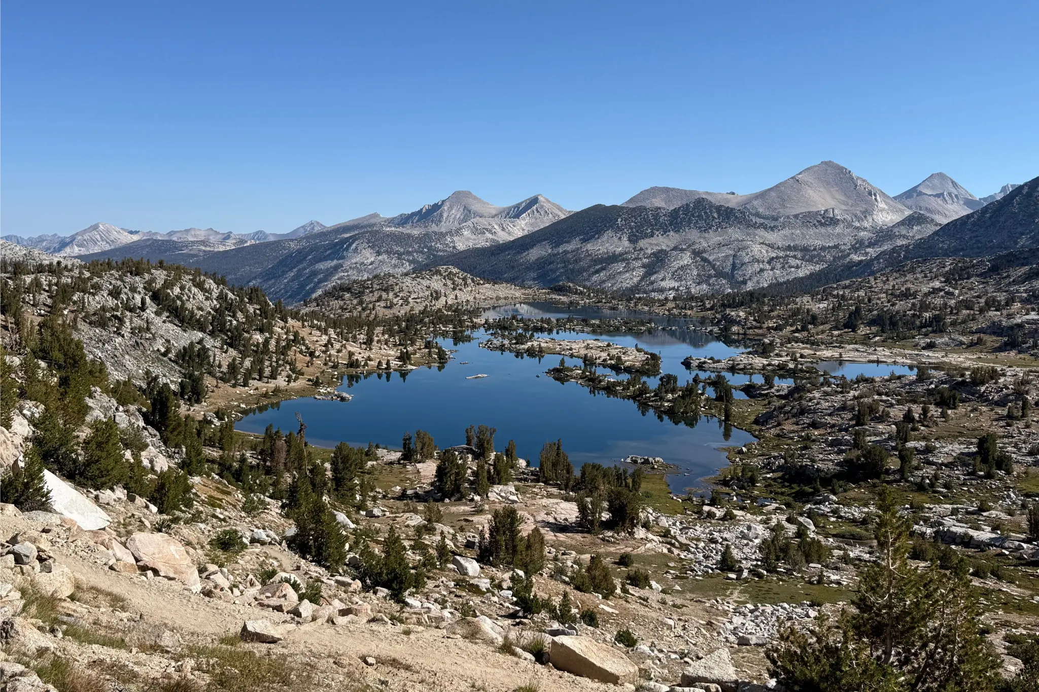 View of lake surrounded by rocks, trees, and mountains.