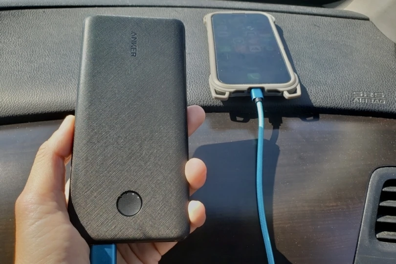 Anker 313 Power Bank in hand while charging a phone on the dashboard