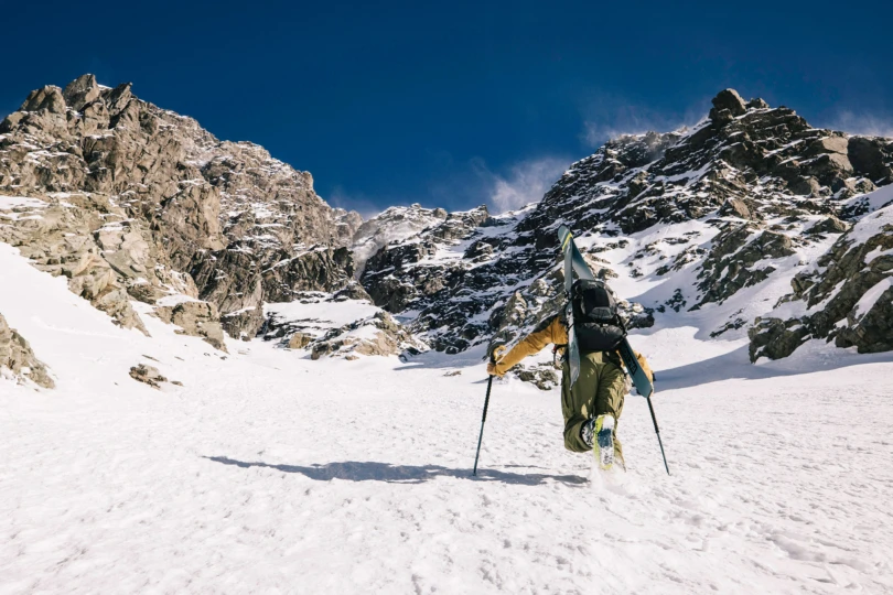 A skier climbs a steep snowy slope with skis strapped to the black Arcteryx Micon LiTRIC backpack
