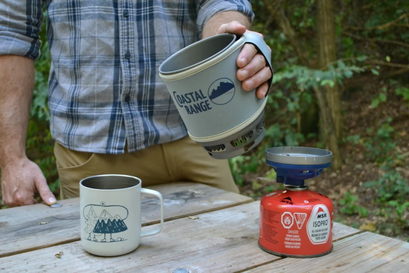 Stove and cup on table with person about to pour water from pot into cup
