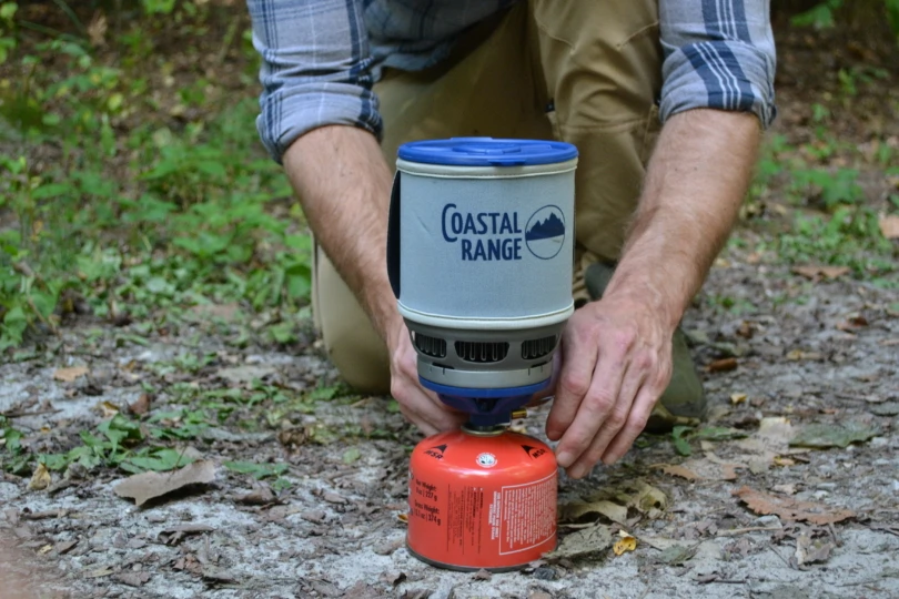 Person kneels while turning on backpacking stove