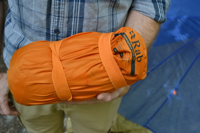 Person holds bundled orange sleeping pad
