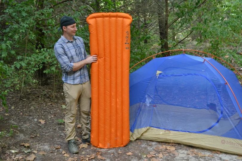 Person stands next to sleeping pad inflated next to tent