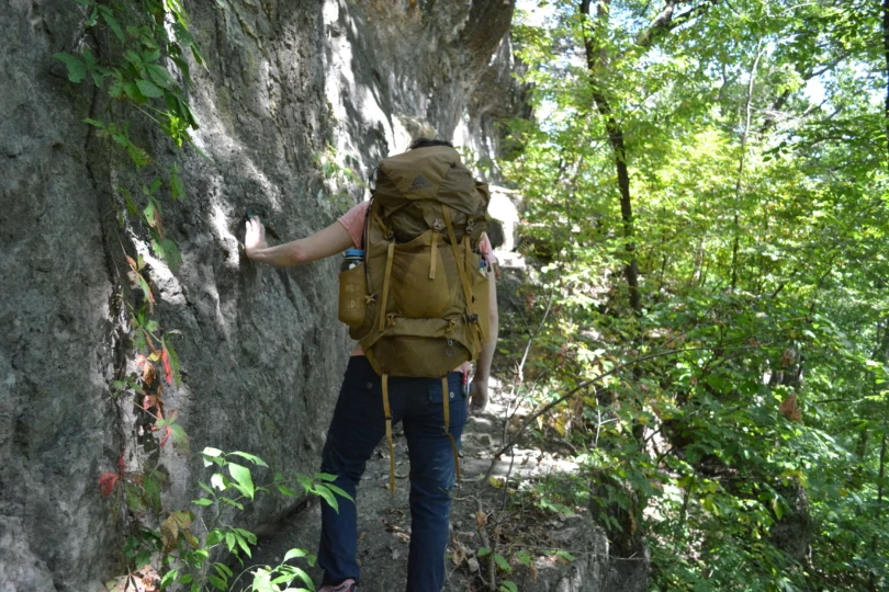 Person wearing brown Gregory pack hikes through rocky forest