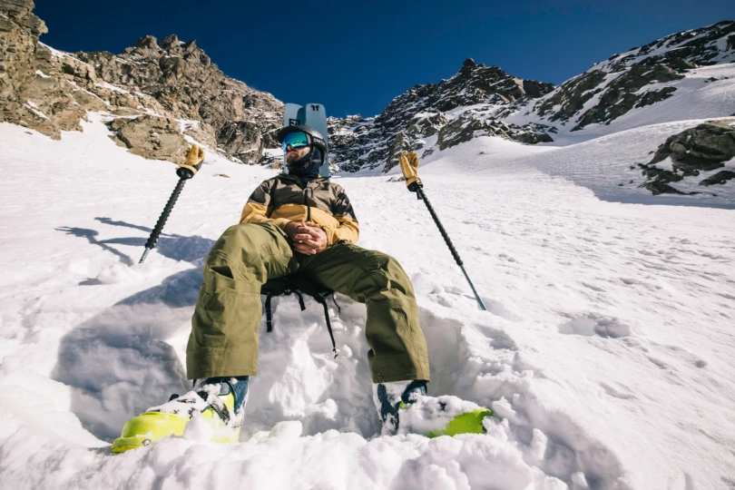 Skier resting on the snow with poles planted, leather gloves on handles