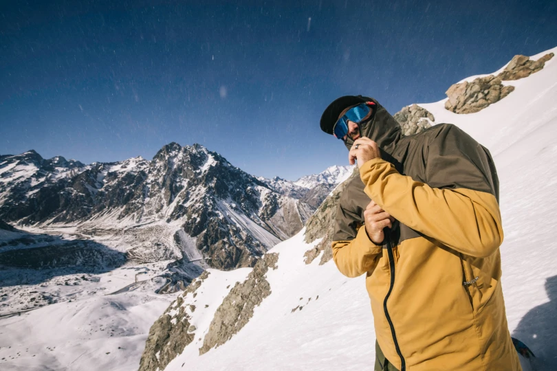 Close-up of skier zipping jacket, reflective sunglasses catching the mountain view
