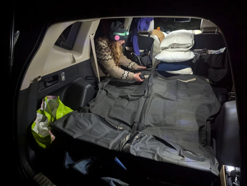 a car camper inflates the luno air pro vehicle mattress in the back of a honda cr-v at night