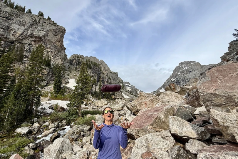 Mountain Hardwear Ghost Whisperer Hoody packed in its stuff sack tossed in the air against mountains