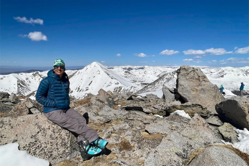 Patagonia Down Sweater Hoody worn while sitting on rocks at a snowy peak