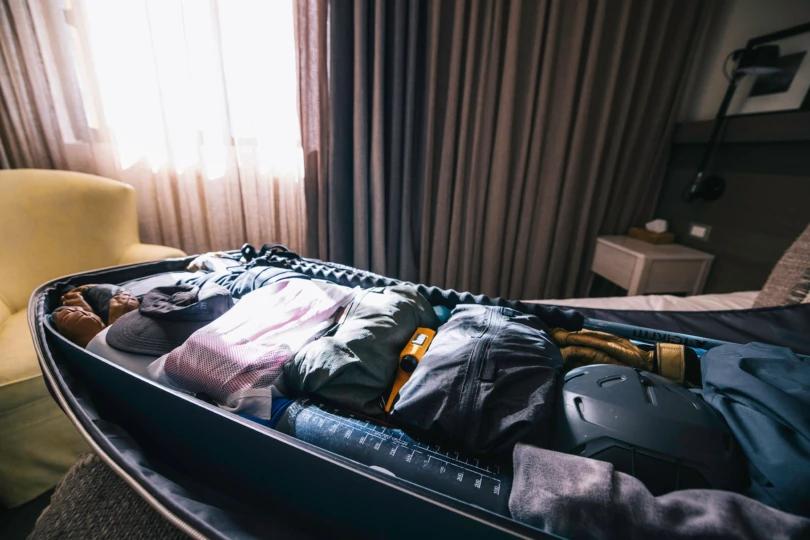 An open ski roller bag on a hotel bed shows organized clothes and gear packed in Peak Design Ultralight Packing Cubes