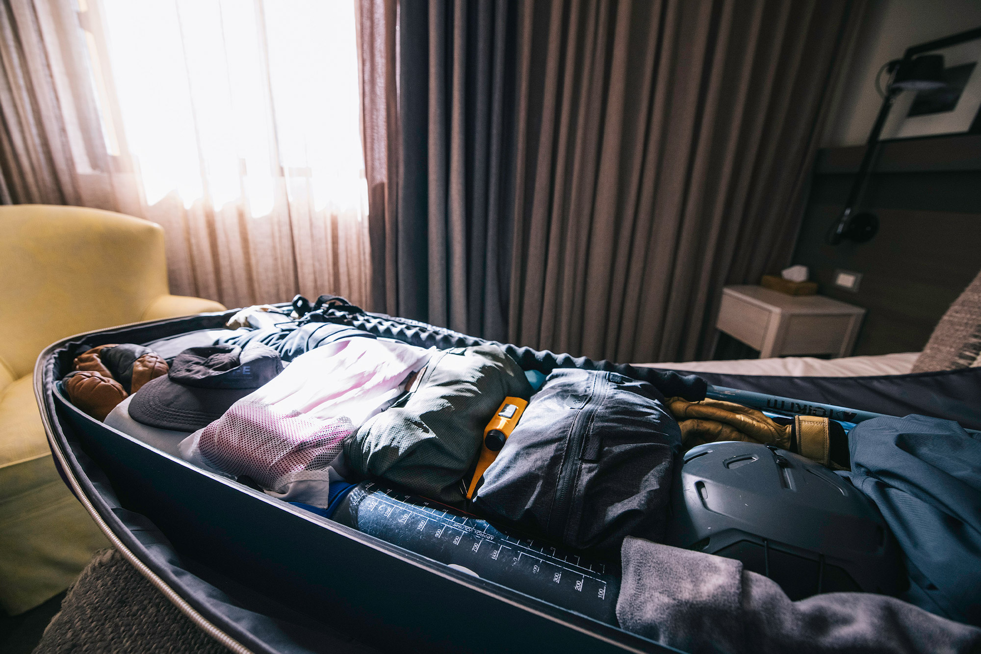 An open ski roller bag on a hotel bed shows organized clothes and gear packed in Peak Design Ultralight Packing Cubes