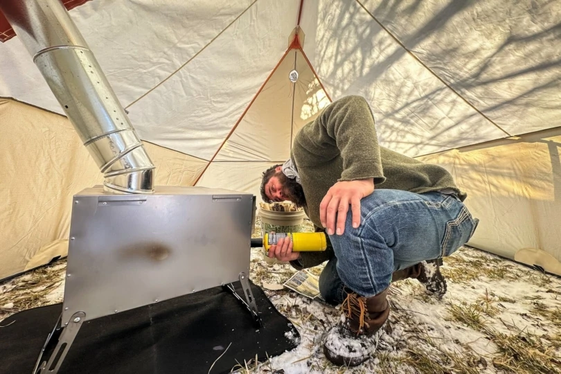 A hunter starts a stove in a hunting tent.