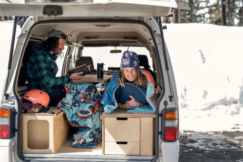 two people sit in back of open van with blankets