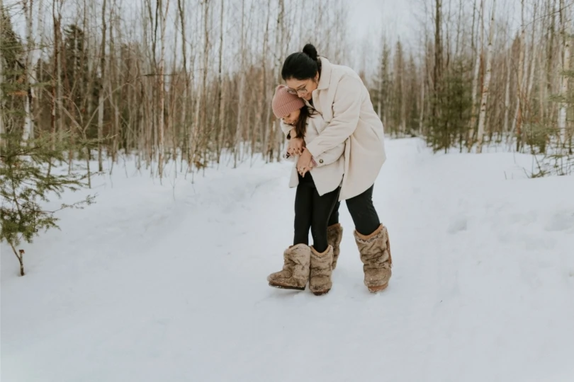 Mamá e hija en nieve con botas peludas