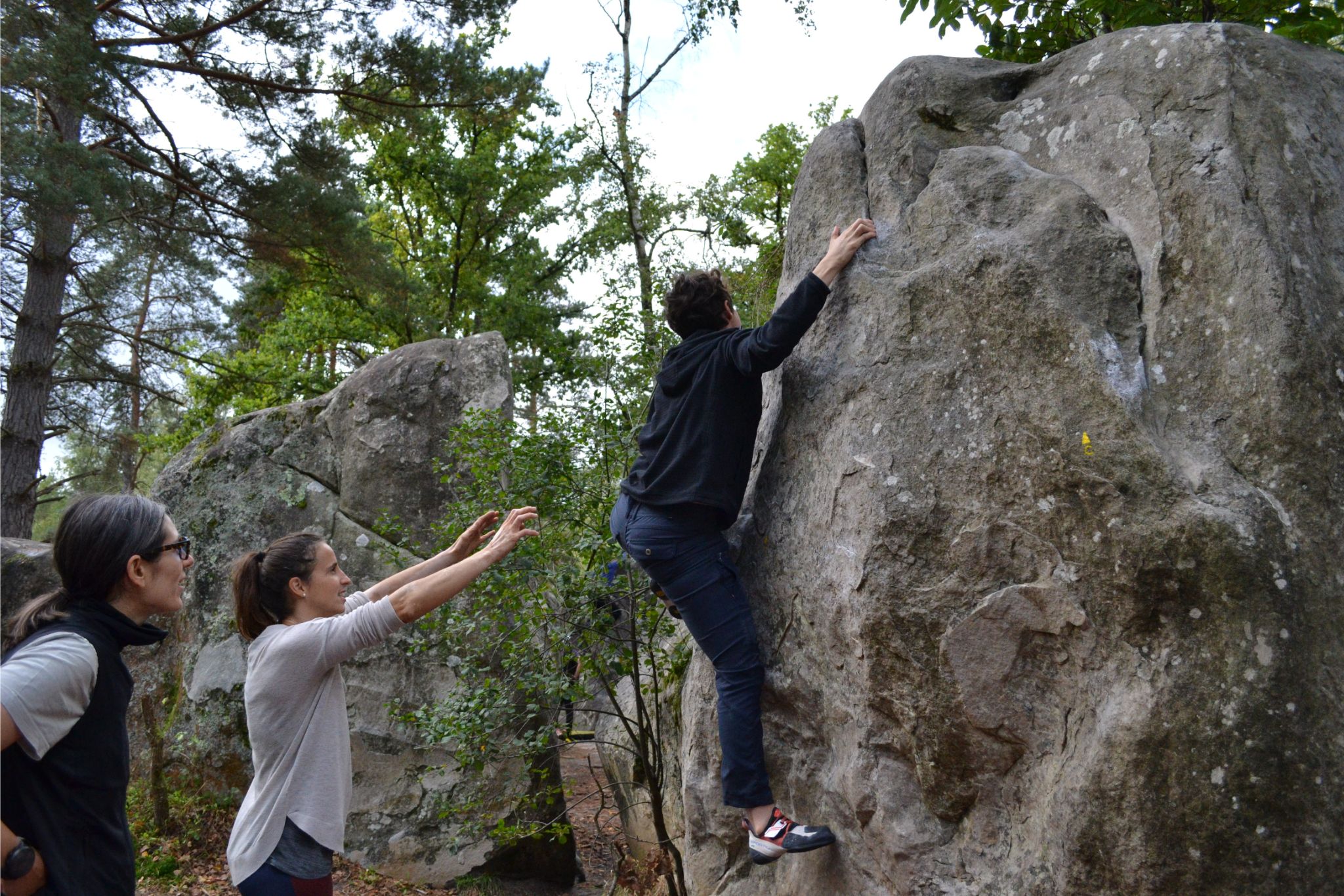 Person climbs up rock with spotters