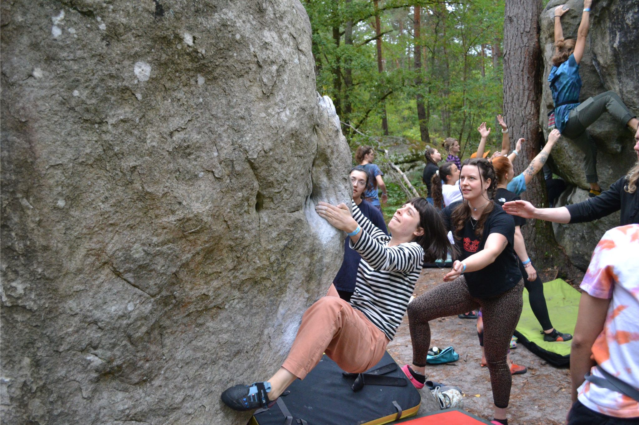 Person climbs up boulder outside with pads and spotters