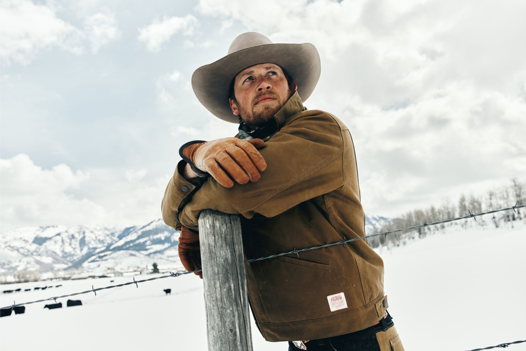 Close up of cowboy leaning on fence in snowy field.
