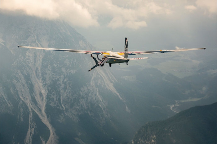 Person climbs on outside of airplane above mountains