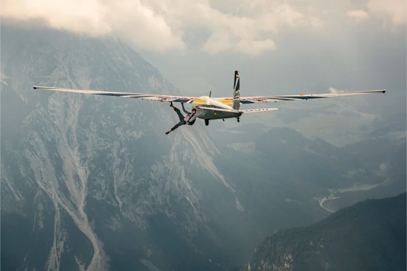 Person climbs on outside of airplane above mountains