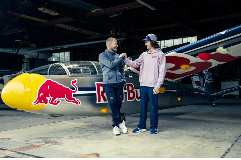 Two people shake hands next to red bull plane