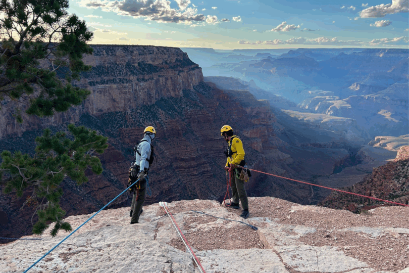 Two people anchored on ropes peer over Grand Canyon edge