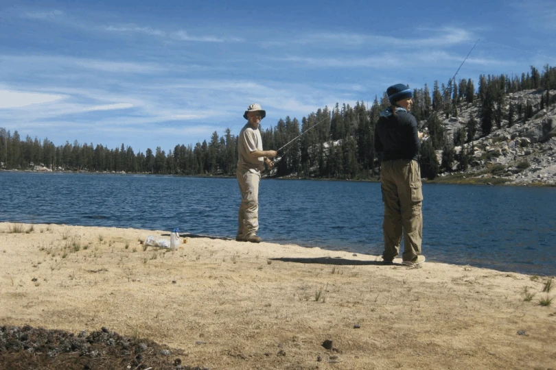 two people fish at sandy lakeshore