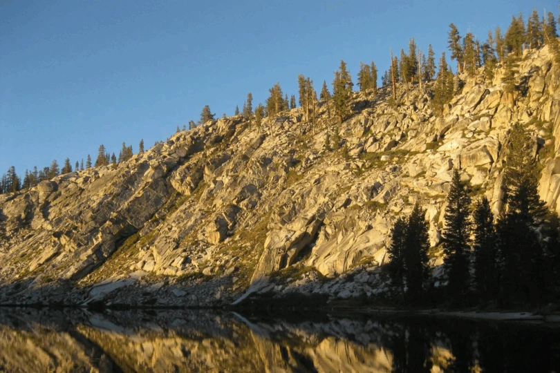 sun comes up over rocky lake