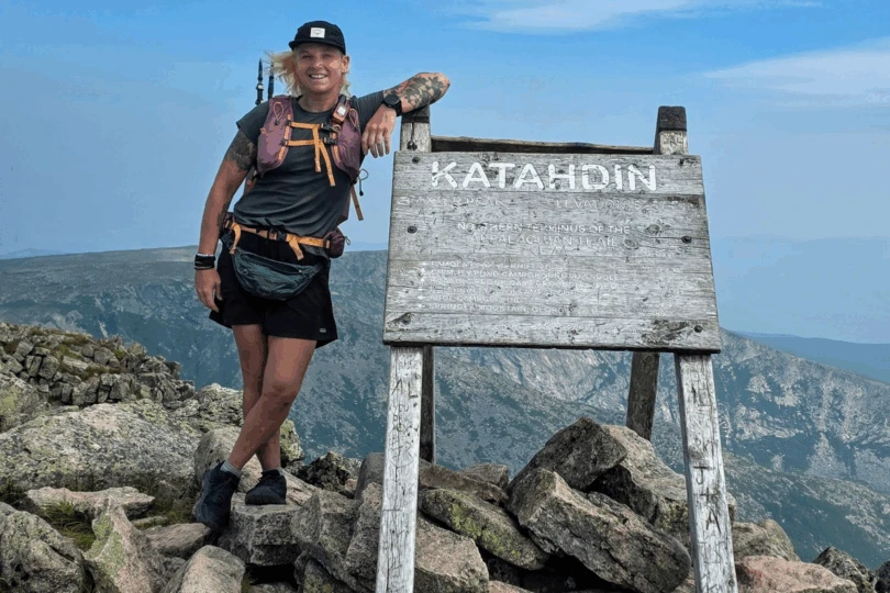 Person stands next to Katadhin sign on moutnain