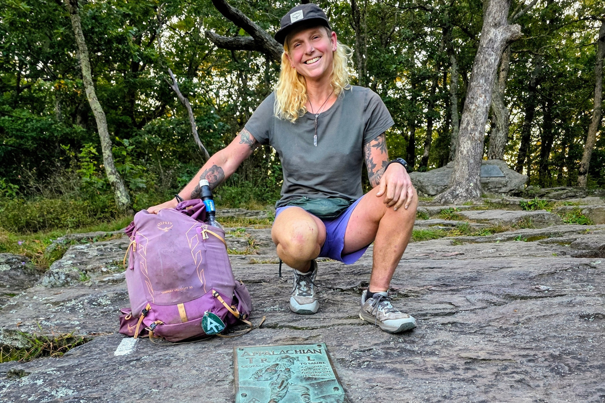 Woman with purple backpack kneels on rock next to AT sign.