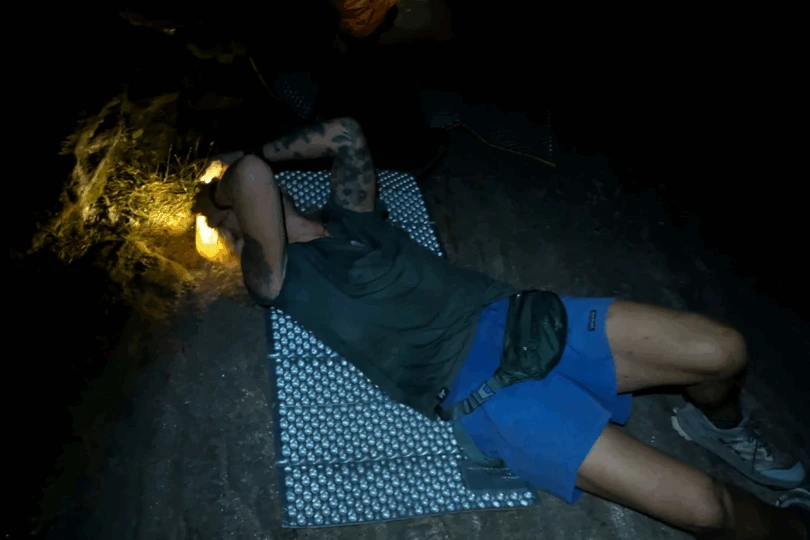 Person lays on sleeping pad on ground in the dark