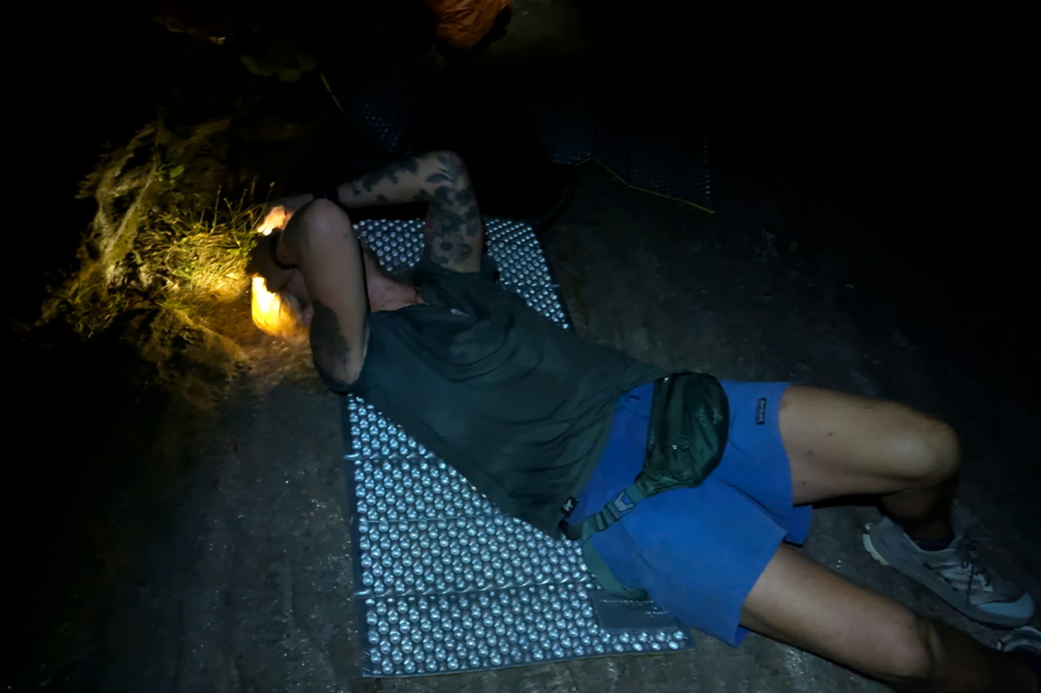 Person lays on sleeping pad on ground in the dark
