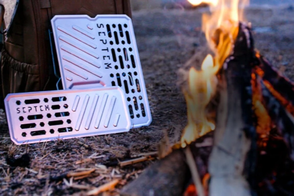 Dos parrillas de metal livianas afuera cerca de una fogata. 