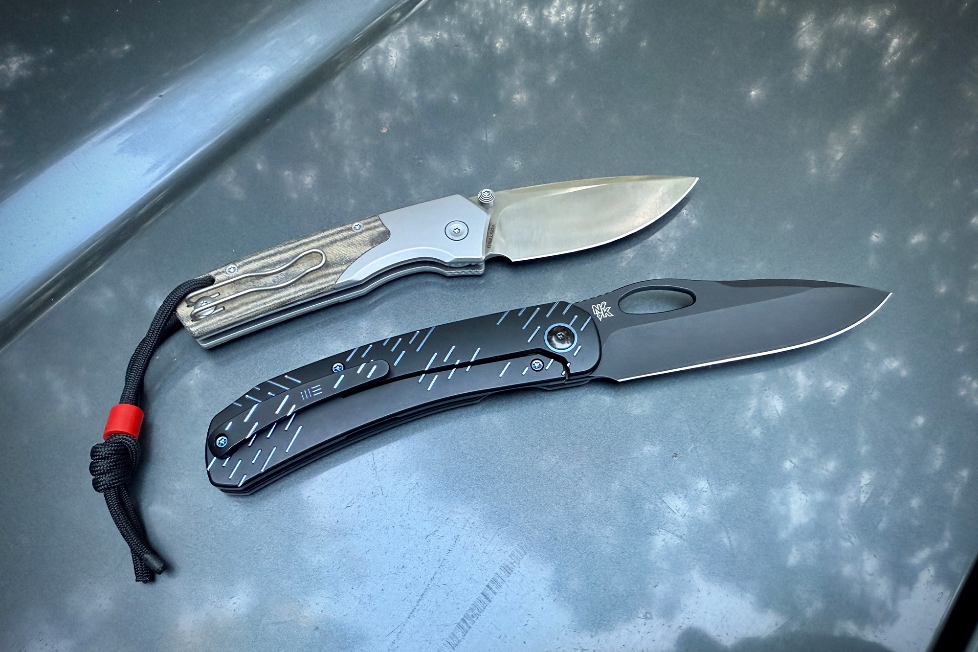 WE Knife Inmate shown next to another folding knife on a car hood