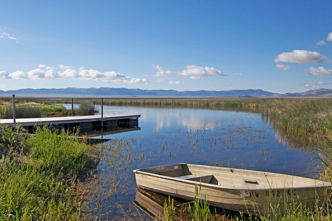 A non-motorized boat is beached along a grassy wetland area in the Ruby Lake National Wildlife Refuge in Nevada.