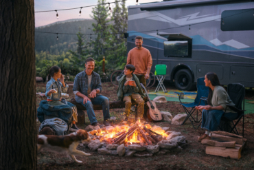 A family sits around a campfire next to their RV in the evening.