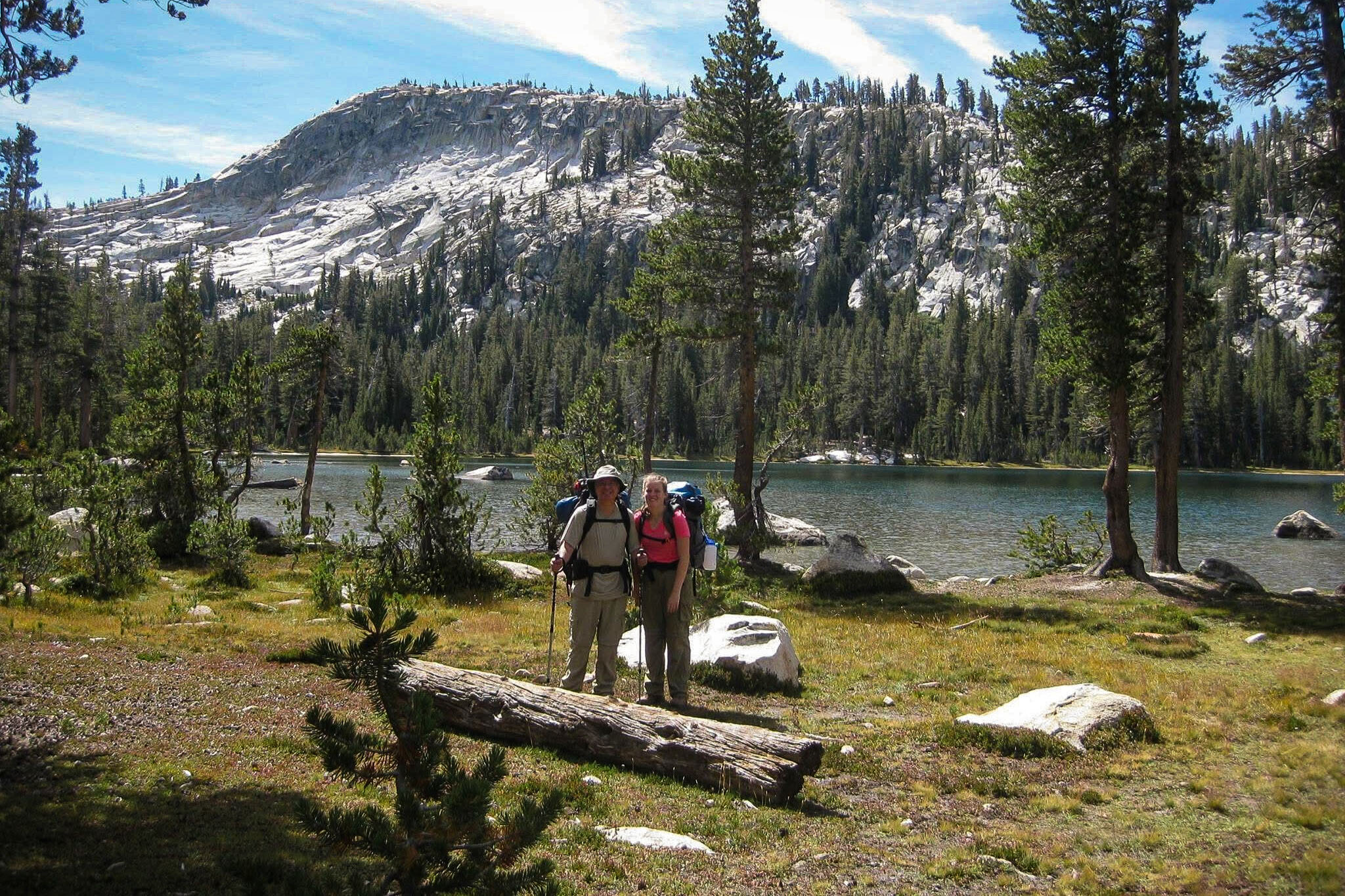 Two people with packs stand in forest in front of lake