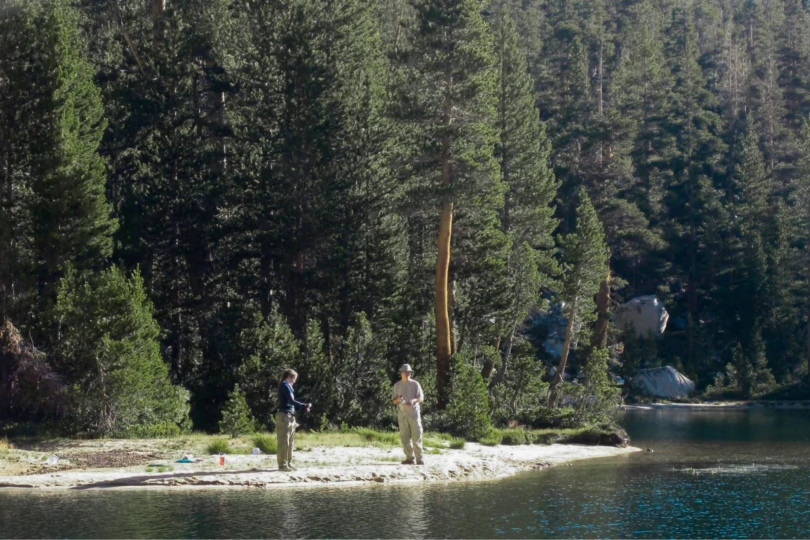 Two people stand on a lakeshore with fishing rods.