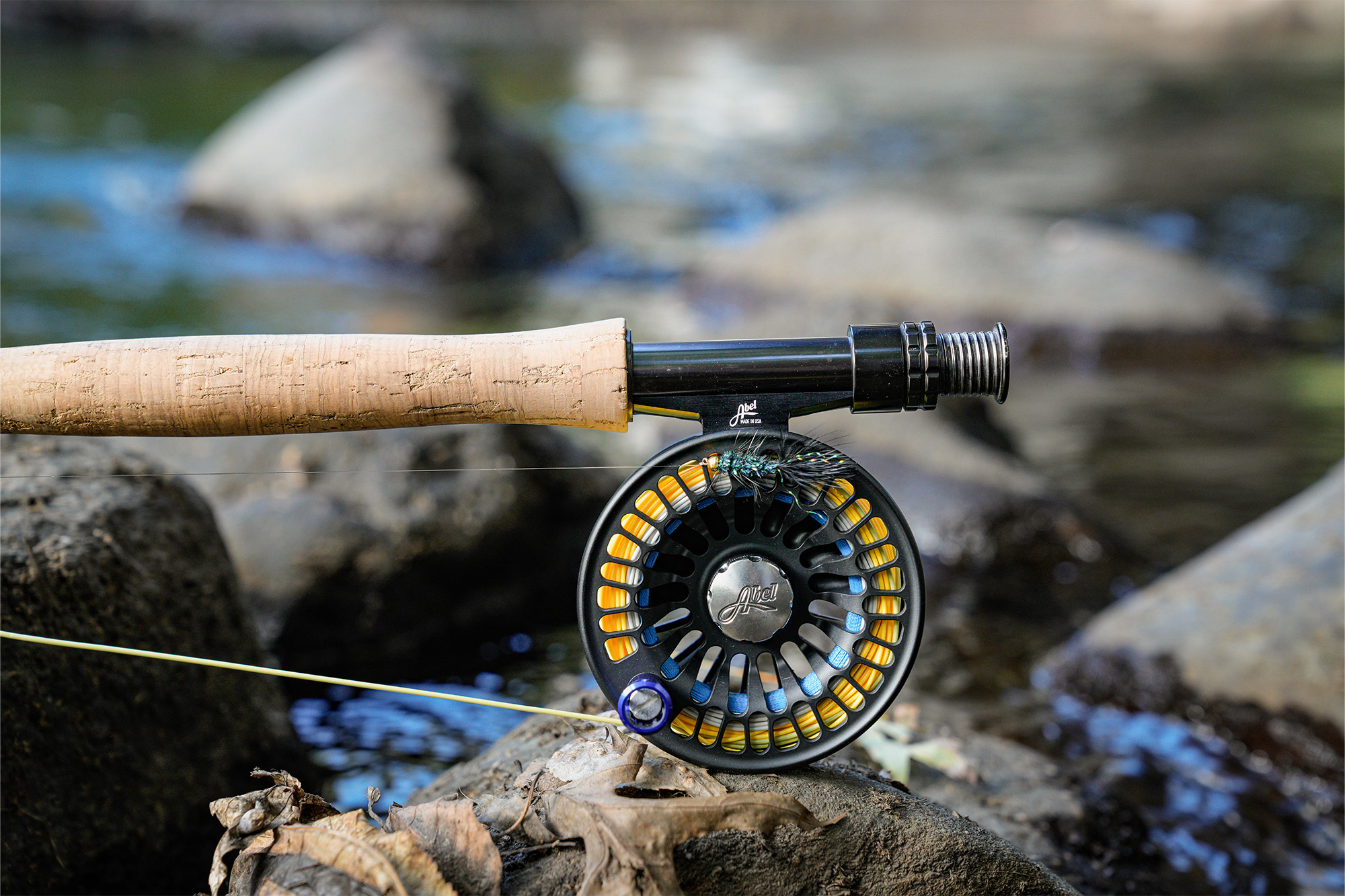 Close-up of the Abel x onWater Custom Reel resting on river rocks beside the water